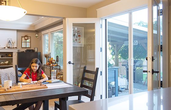 Young girl sitting at table in front of retractable door screens